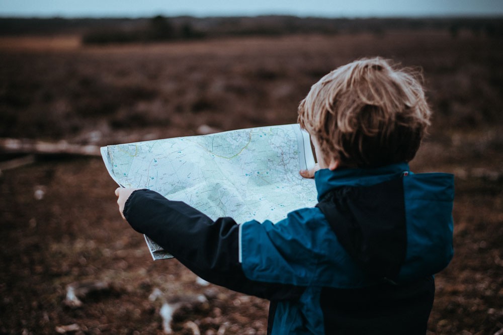 niño rubio con un anorak mirando un mapa