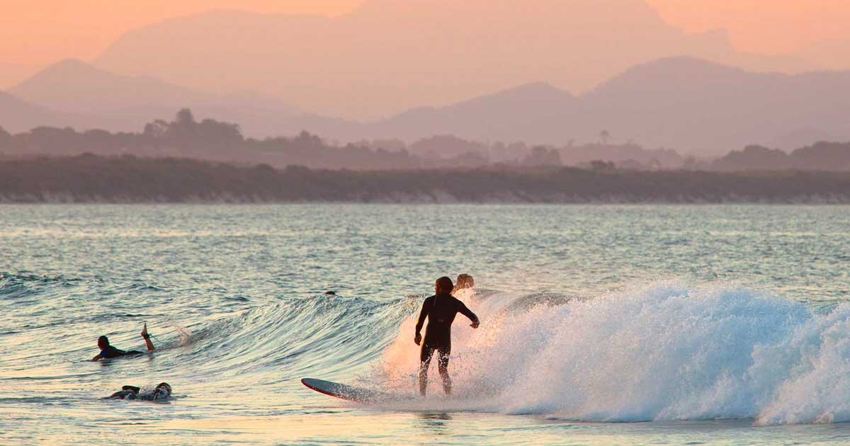 puesta de sol y un chico haciendo surf en una playa y de fondo la vegetación 