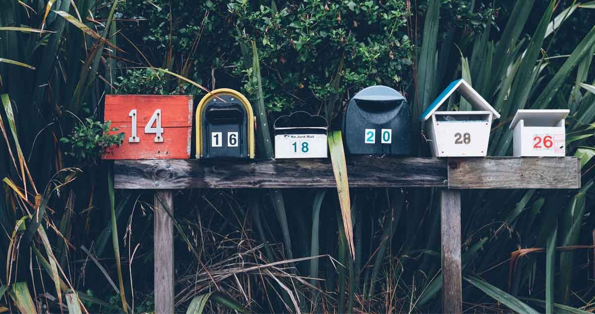 buzones de correo postal de madera y de diferentes medidas y colores encima de una madera en medio de la vegetación