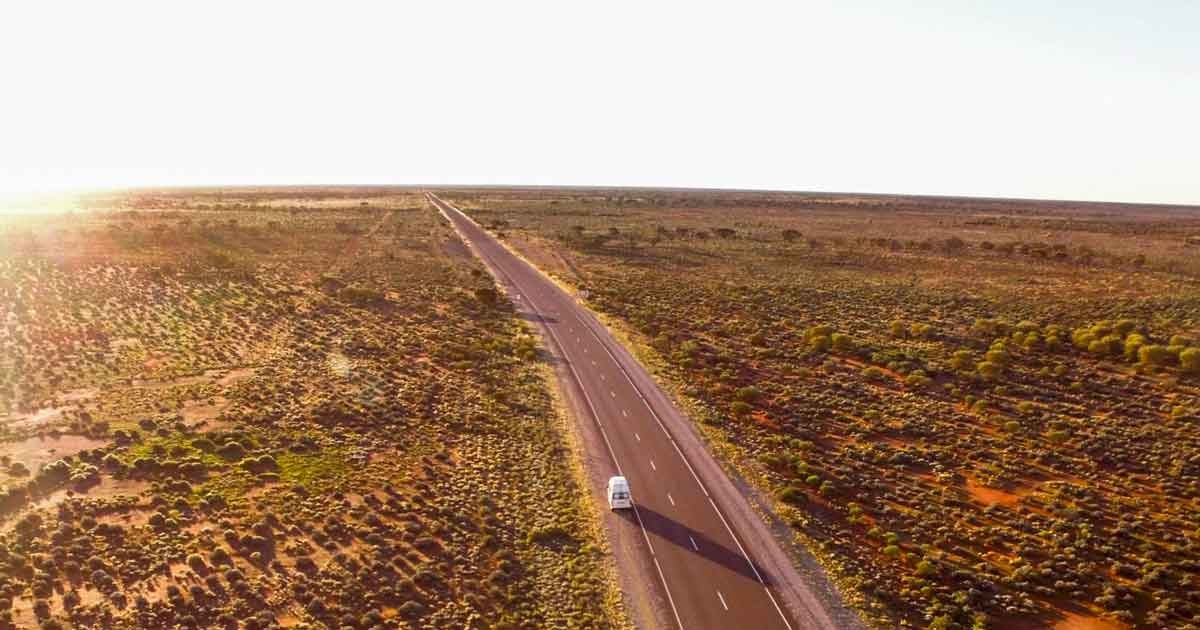 fotografía aérea de una carretera con una caravana y la puesta de sol