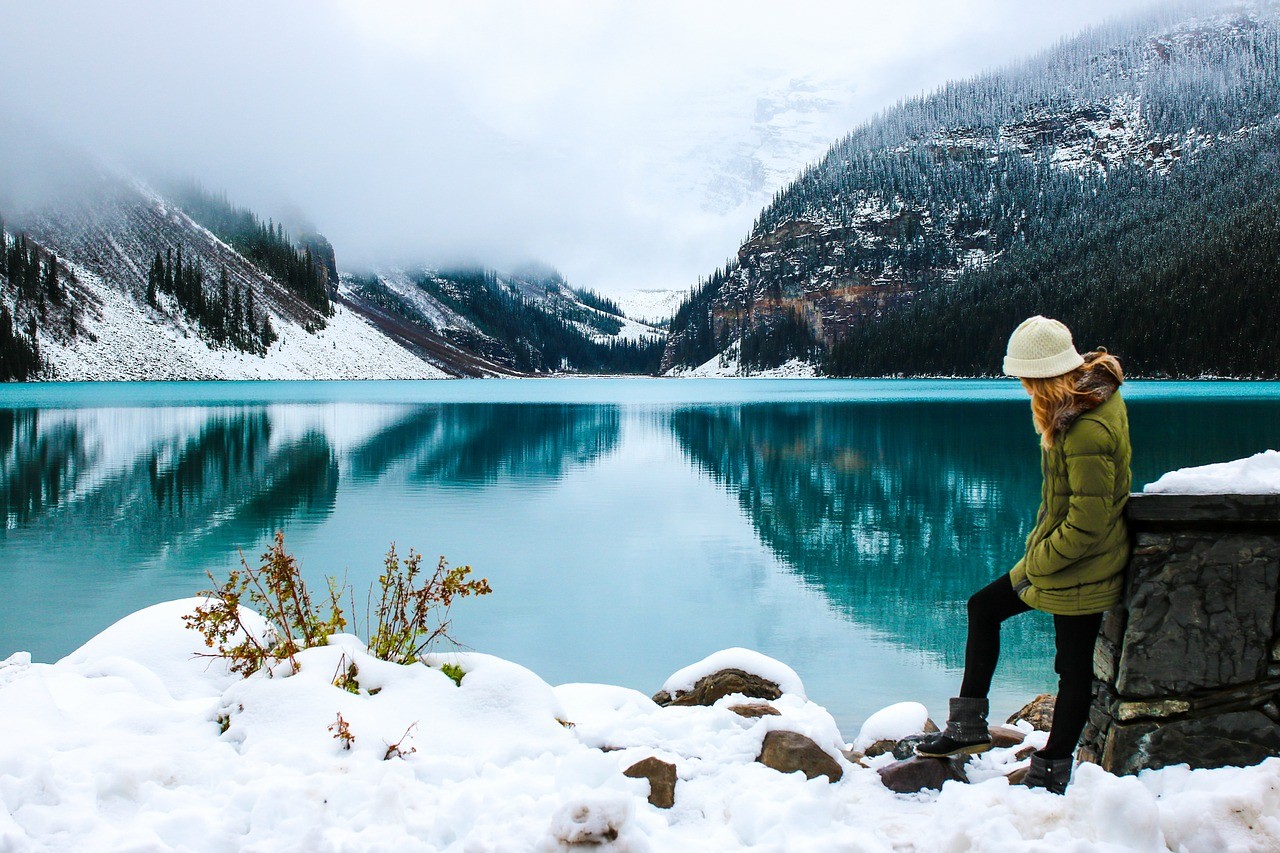 chica abrigada encima de la nieva al lado de un lago rodeado de montañas