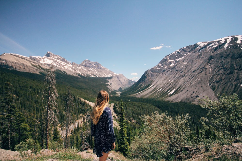 chica rubia de espaldas y delante el paisaje de las montañas de Canadá