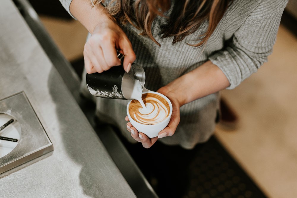 fotografía de unas manos de una chica haciendo una figura con la leche en un café