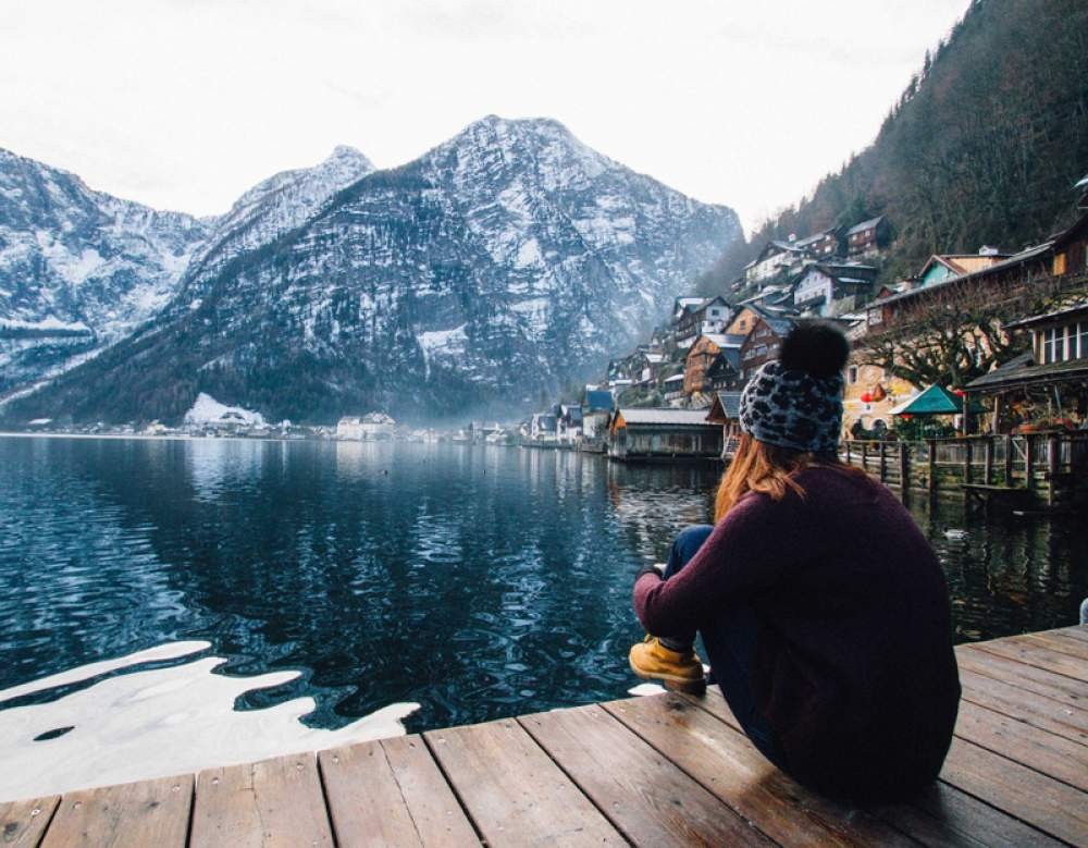 chica con gorro de lana de espaldas sentada en un muelle contemplando el paisaje montañoso de Canadá