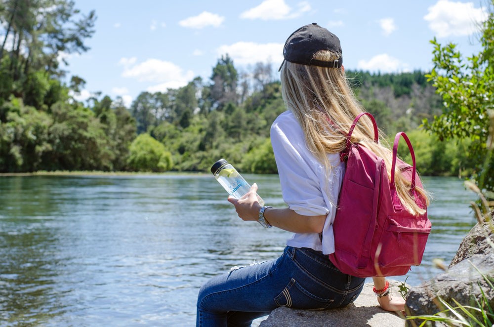 chica rubia de espaldas sentada en una roca de un lago