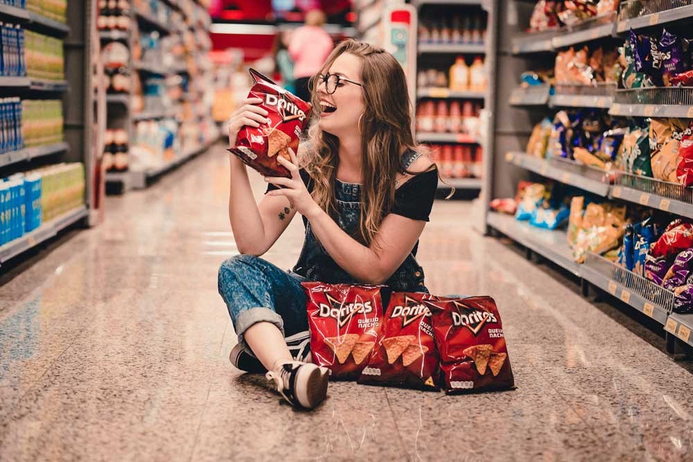 chica sentada en el suelo de un supermercado con bolsas de Doritos