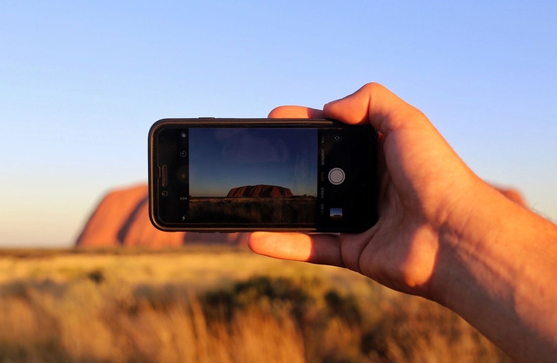 Mano sujetando un teléfono que hace fotografía al uluru de Australia