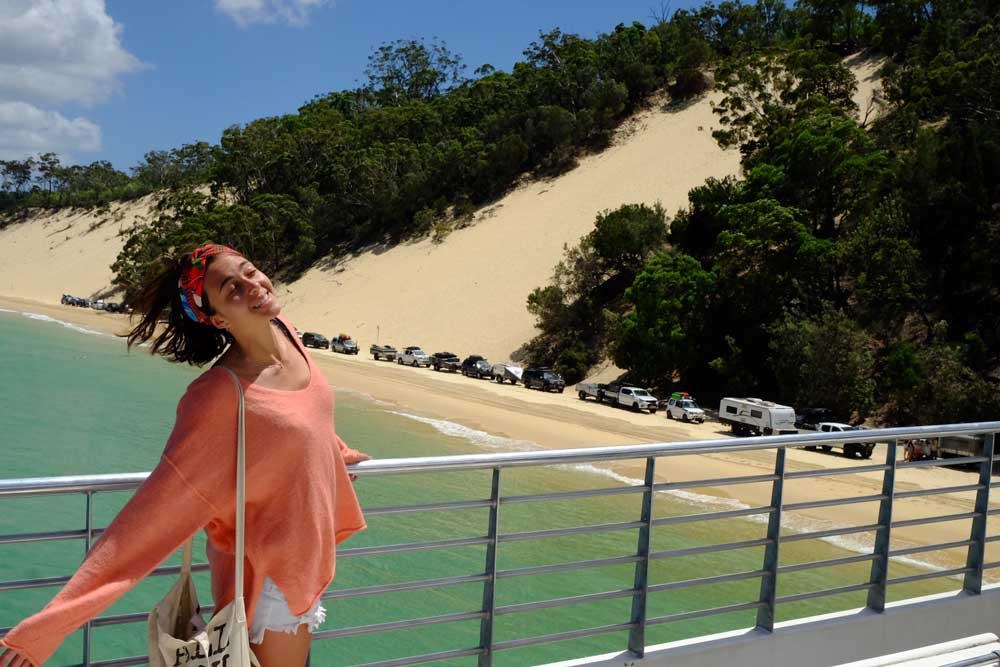 chica morena en un puente y detrás la playa y montañas