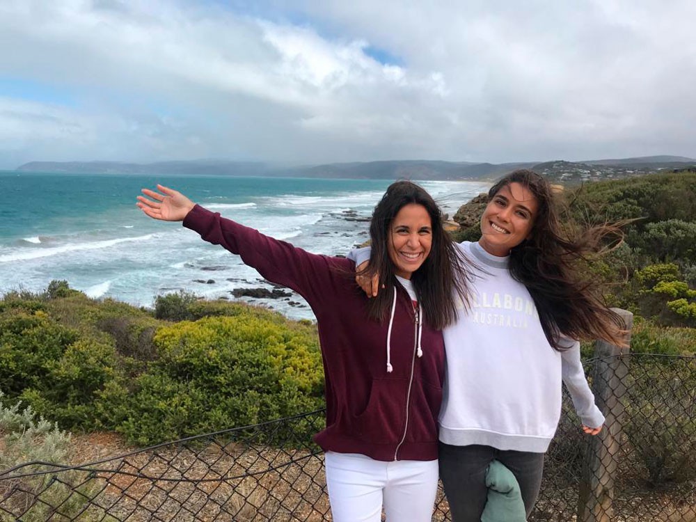 dos chicas morenas sonriendo a cámara y detrás la playa