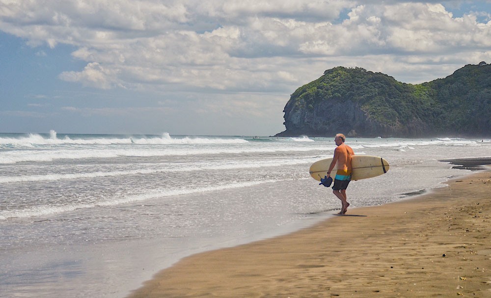 neozelandés con una tabla de surf en la orilla de una playa