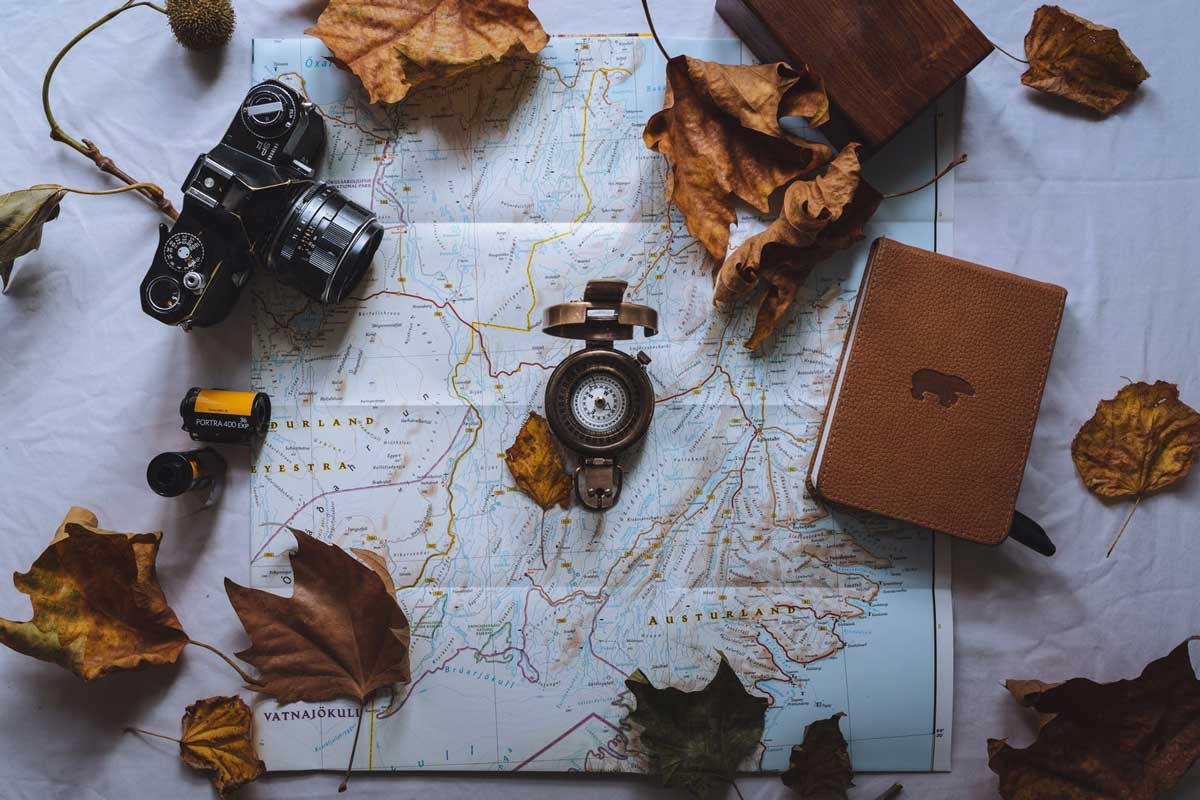 cámara, carretes de fotos, brújula, libreta y caja de madera encima de un mapa en una mesa con hojas marrones