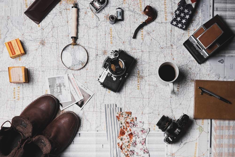 fotografía de un mapa y encima objetos básicos para viajar como una cámara, zapatos, lupa, fotografía