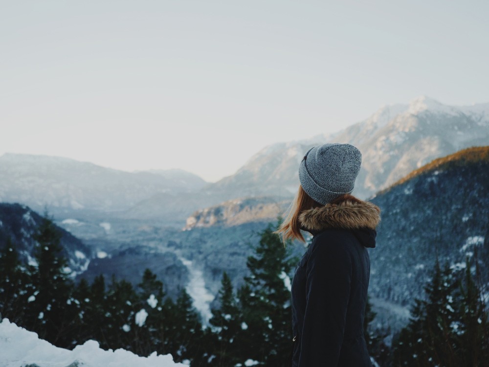 chica con un gorro gris de lana de espaldas mirando el paisaje de naturaleza de canadá