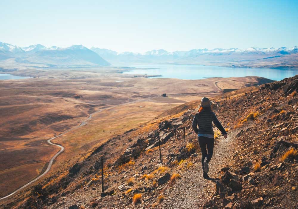 chica de espaldas andando por una montaña y al fondo un lago