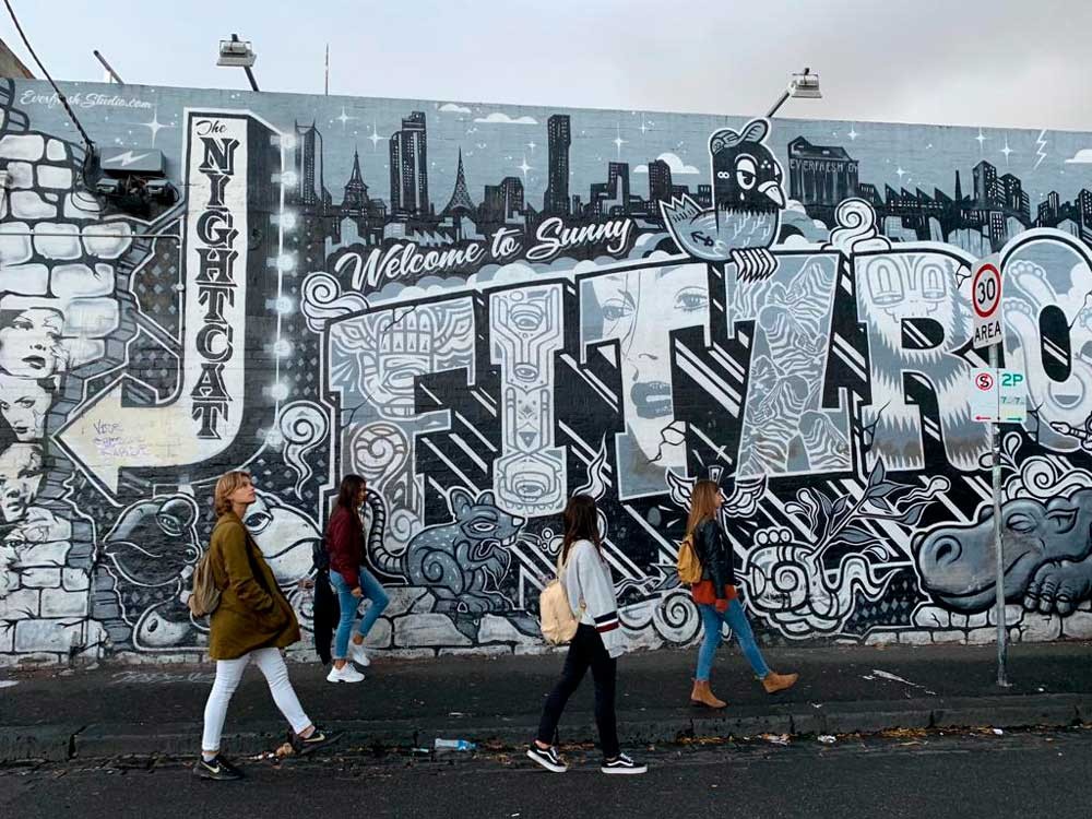 cuatro chicas andando de perfil y detrás tienen una pared con graffities