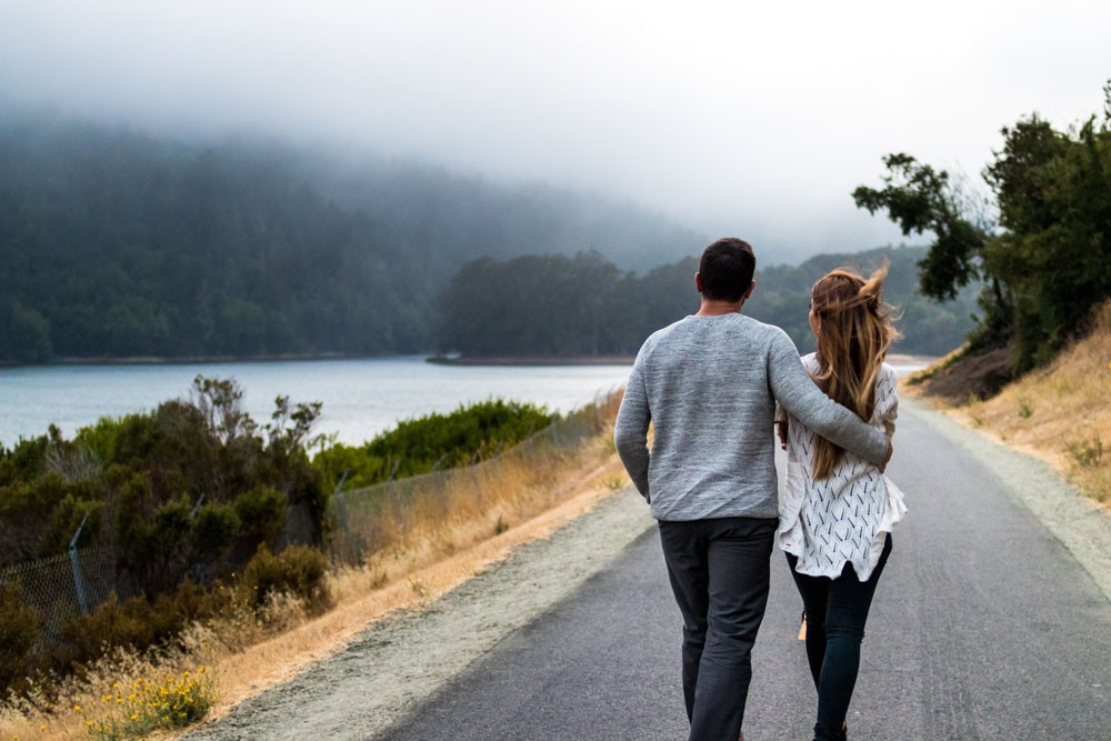 pareja andando por una carretera y delante el paisaje de una montaña con el lago