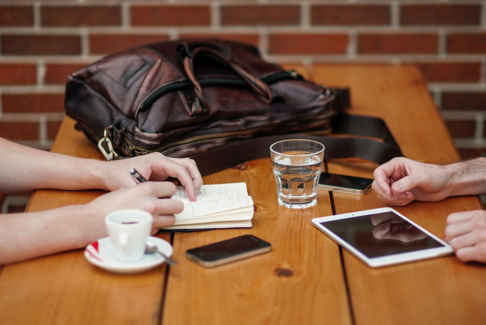 chico y chica en una mesa de madera con un bolso encima y un café 