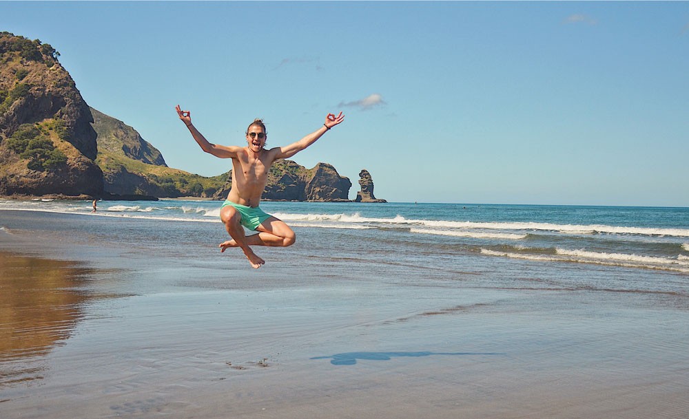 chico moreno con bañador saltando en la orilla de la playa