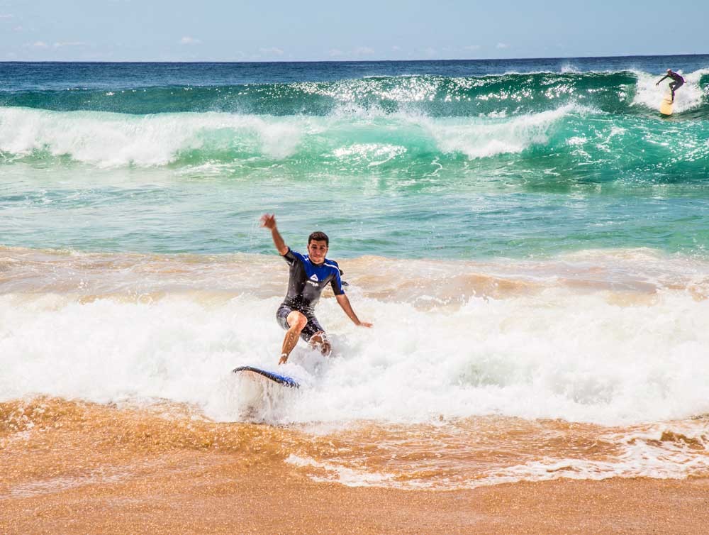 chico con el traje de neopreno surfeando en una playa