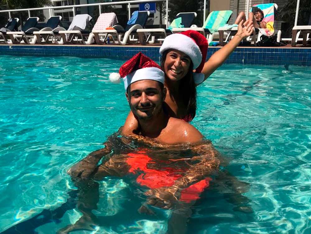 una chica encima de un chico morena en la piscina con un gorro de navidad