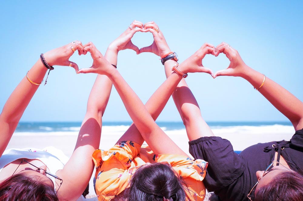 Tres chicas en la playa haciendo corazones