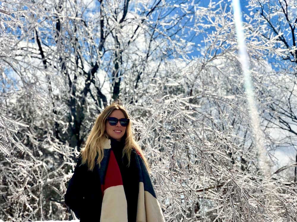 chica rubia con unas gafas de sol y una bufanda y detrás el paisaje nevado